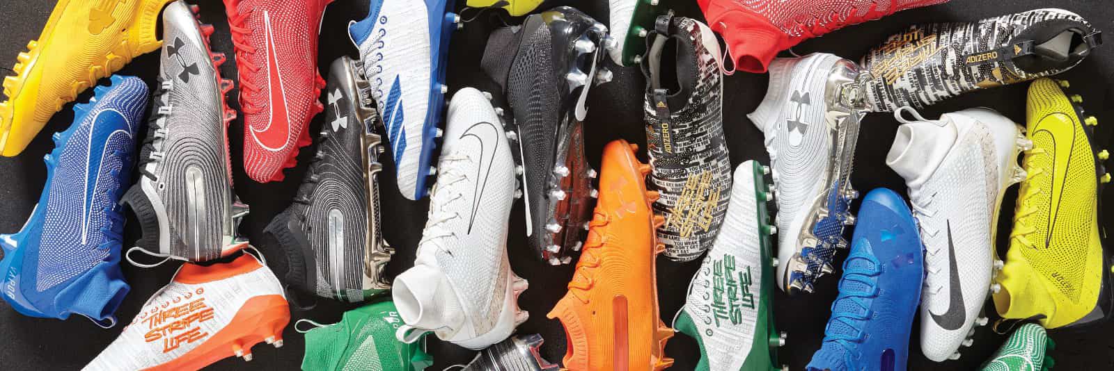 A collection of football gear including Nike Cleats, Under Armour Gloves, a Wilson NFL football, & a Shock Doctor lip guard in a variety of colors.