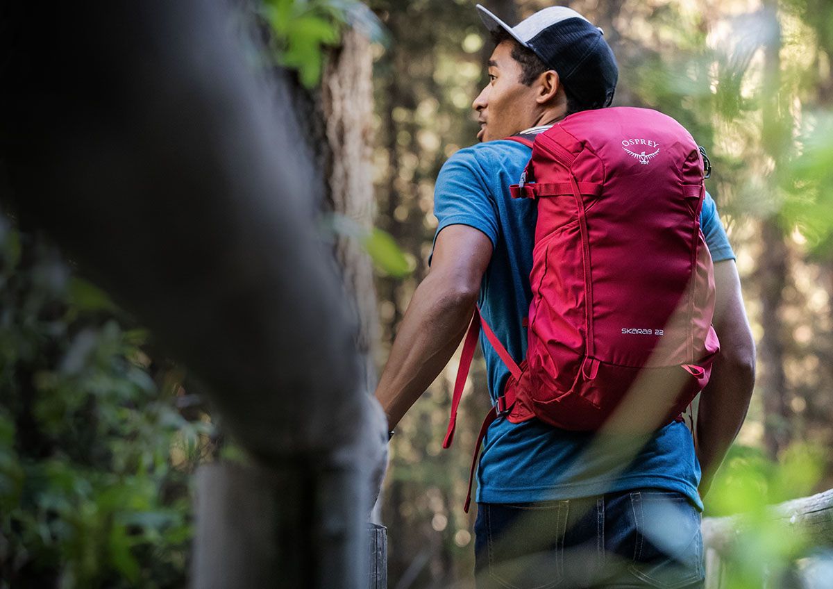 A man on a hike through the woods, looking up over his left shoulder while wearing an Osprey 10001885 22 backpack.