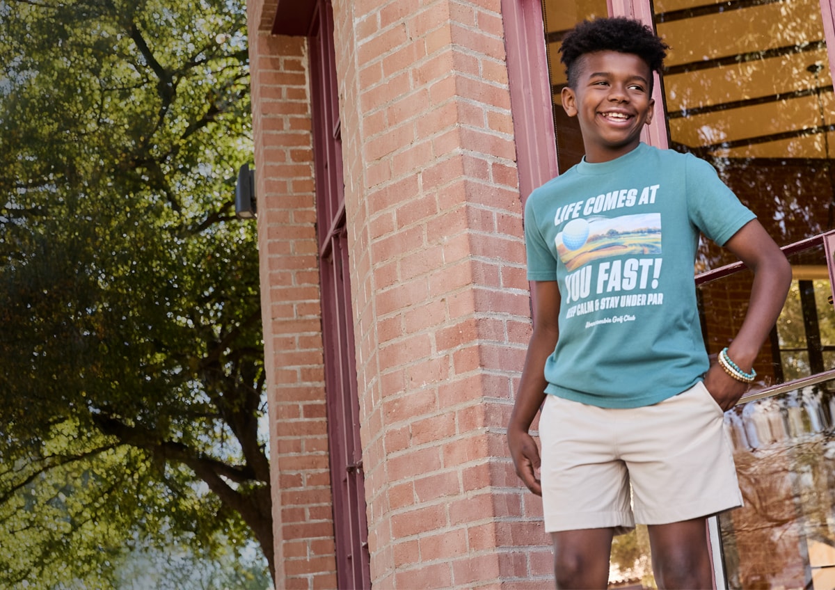 Boy imtee and shorts standing outside.