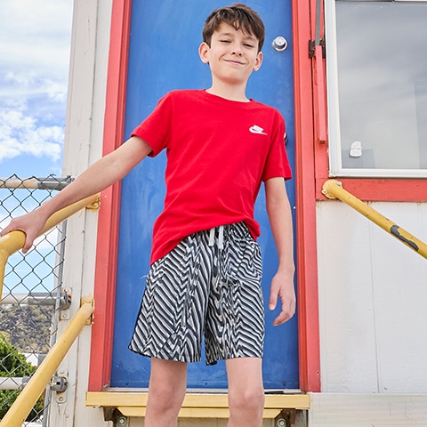 Boy in tee and shorts standing outside.