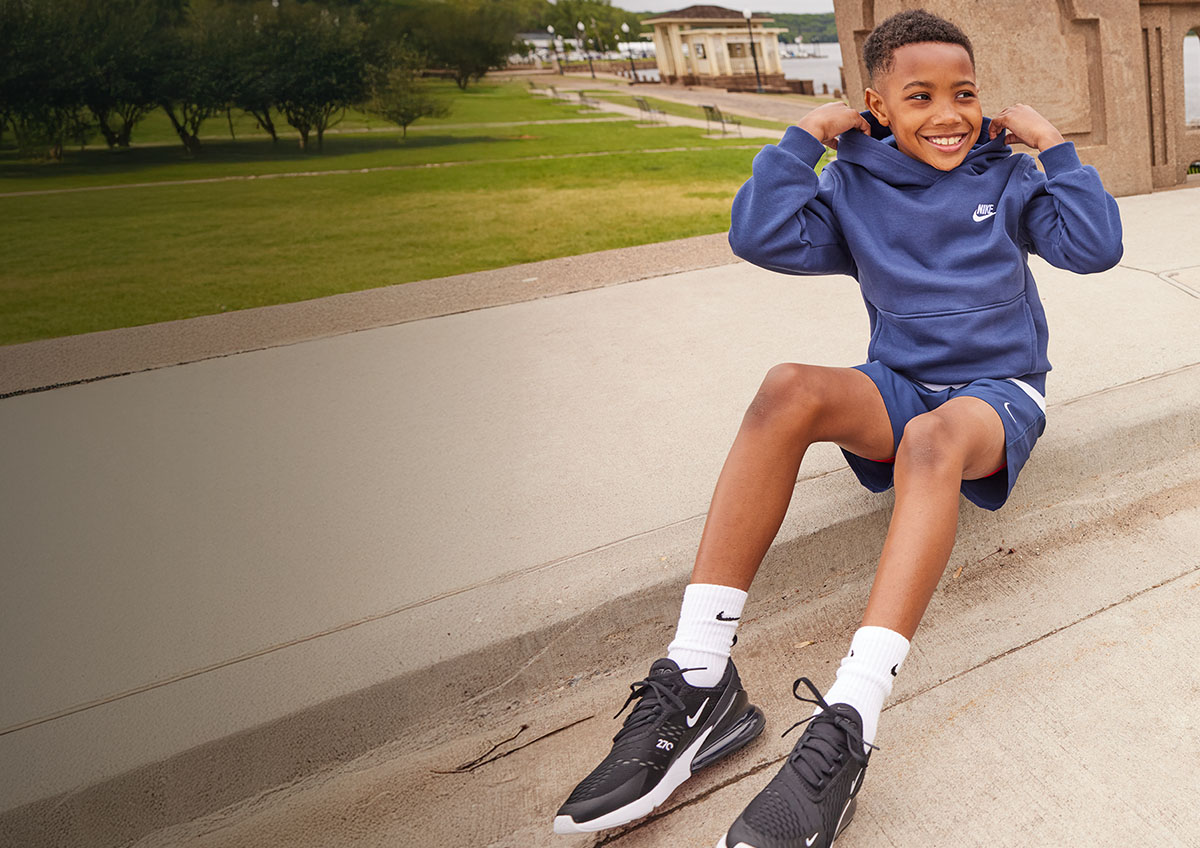 Boy sitting on side walk adjusting his hoodie.