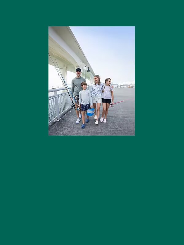 Family with fishing gear in hand, walking together next to a bridge.