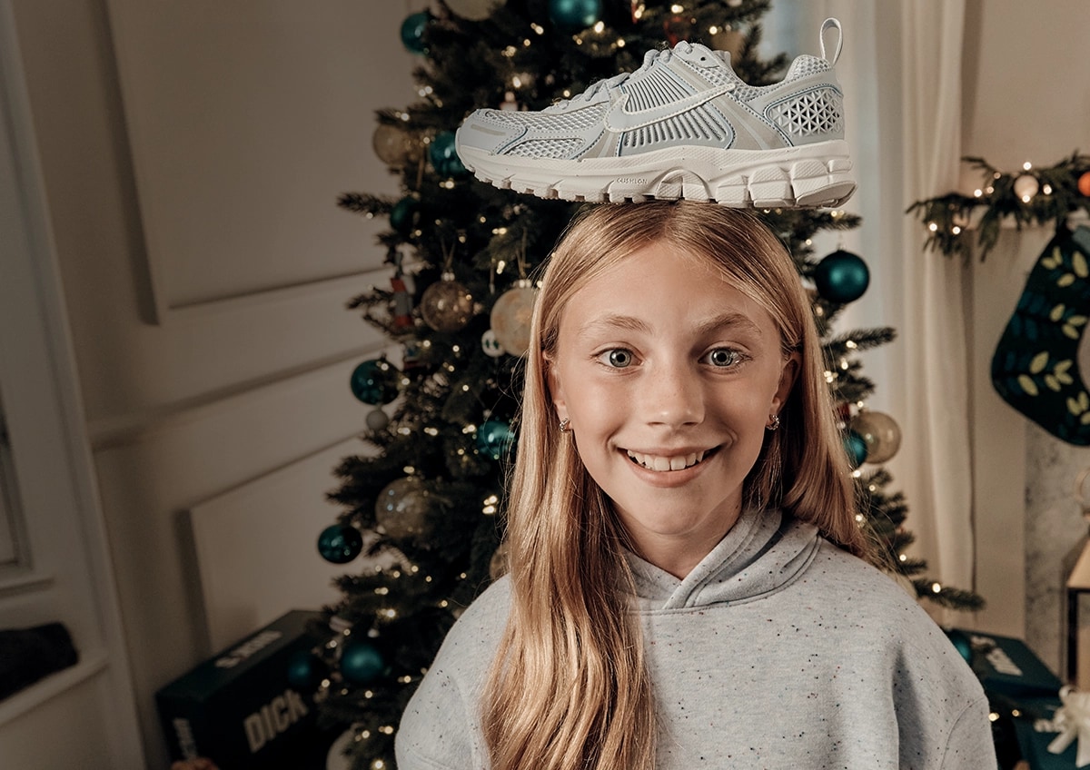 Girl in front of a Christmas tree with a shoe on his head.