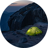 green tent on a rocky cliff at night
