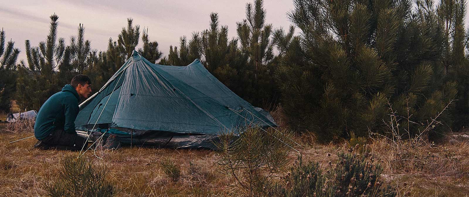 A man setting up his tent near surrounding evergreens.