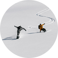 Two snowboarders carving down a mountainside.