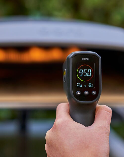 A man taking the temperature of an Ooni pizza oven.