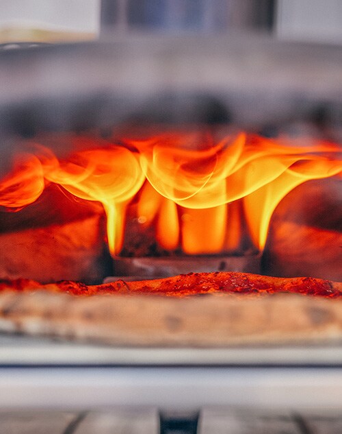 A pizza being cooked by an Ooni outdoor gas oven.