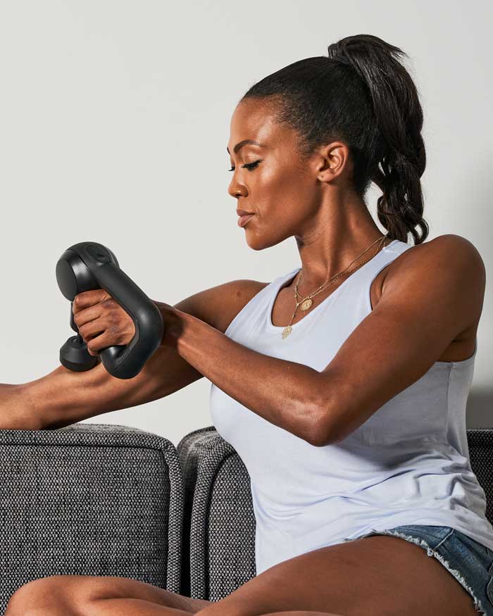 woman sitting on couching using theragun on bicep