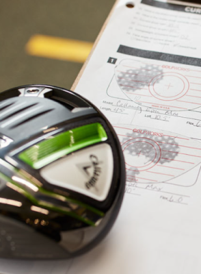 The head of a golf club, with the Calloway logo reflected upon it, rests against a Golfworks worksheet